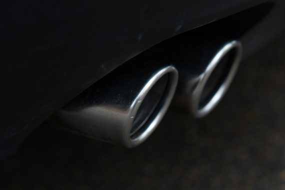 Closeup shot of the exhaust pipe of a black car against a background of sark asphalt